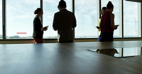 Office team in suits exchanging information using smart devices at conference table, with city view