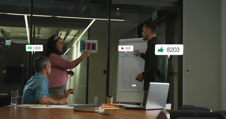 Analyzing metrics, three colleagues pointing at color chart in glass conference room, with laptop