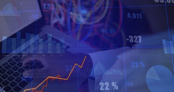 Business executive in suit entering data on laptop at office desk, with financial chart overlays - Powered by Adobe