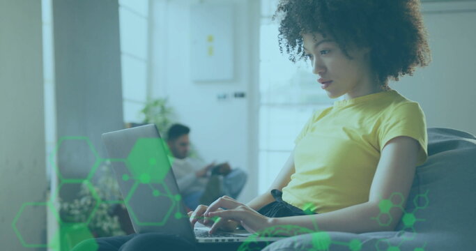 Typing woman using laptop in living room, with potted plant and man using smartphone, copy space