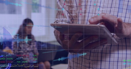 Standing male manager holding stylus and tablet reviewing charts in office, with floating tickers