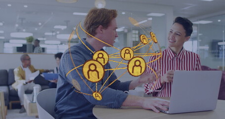 Typing two office workers collaborating at shared workspace with silver laptop and network graphic