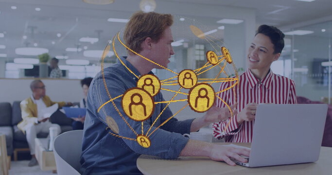 Typing two office workers collaborating at shared workspace with silver laptop and network graphic - Powered by Adobe