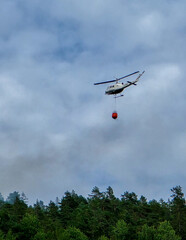 Fototapeta na wymiar Helicopter battling wildfires in Norway with a water bucket during summer