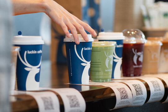 KUALA LUMPUR, MALAYSIA - AUG 17, 2025: Close up of a barista placing takeaway drinks from Luckin Coffee on the counter with printed order receipts.