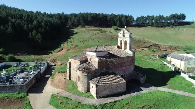 Ancient stone church in Nogales de Pisuerga beside a cemetery and forested hillside