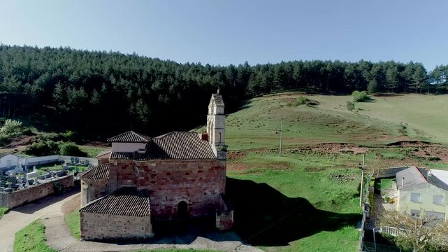 Ancient stone church in Nogales de Pisuerga beside a cemetery and forested hillside
