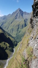 Mountain valley vista, steep cliff edge, lush greenery, distant peak