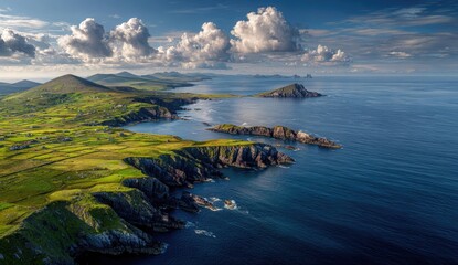 Panoramic coastal view of Ireland's rugged coastline, with rolling hills, green pastures, and dramatic cliffs meeting the azure ocean. Large, fluffy clouds are scattered across a vibrant blue sky