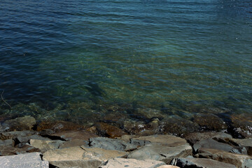 Clear water of a lake with visible rocks on the shore. Natural background with blue and green transparent water and stone coastline.