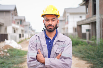 Engineer or worker at housing site smiling with arms crossed, showing confidence.