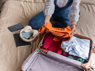 A beautiful Asian traveler woman sits packing her suitcase on a bed in a hotel room