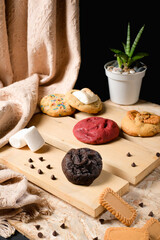 Variety of thick cookies on wooden boards—front focus on rich chocolate cookie—styled with marshmallow, chocolate chips, and dark backdrop for tempting bakery advertising visuals.