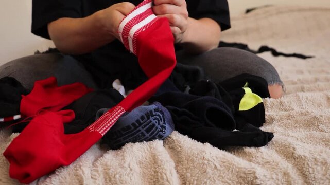 In a cozy bedroom, a woman carefully folds various articles of clothing while sitting cross-legged on a soft surface. She focuses on organizing her laundry with attention