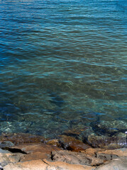 Clear water of a lake with visible rocks on the shore. Natural background with blue and green transparent water and stone coastline.