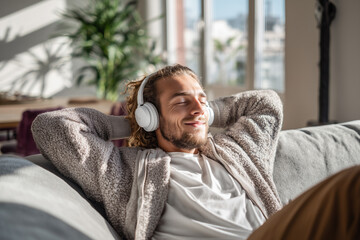 Happy man listening music while relaxing on sofa at home. Lifestyle and leisure time concept