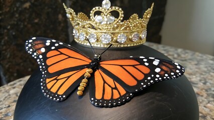 a monarch butterfly perched on black sphere wearing golden crown