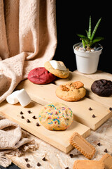 Assorted soft-baked cookies—chocolate, red velvet, speculoos and marshmallow—arranged on rustic boards with chocolate chips; clean studio still life for bakery marketing and packaging.