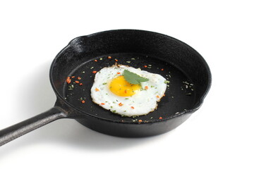 On a white background there is a cast iron frying pan with a fried egg.	