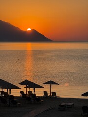sunset on the beach Golden Sunset Over Serene Beach with Straw Umbrellas and Lounge Chairs