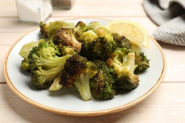 Tasty fried broccoli and lemon on light wooden table, closeup