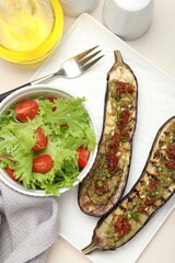 Slices of grilled eggplant with sun dried tomatoes, pesto and salad on white table, flat lay