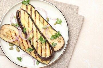 Slices of grilled eggplant, parsley, pumpkin seeds and onion on white table, top view. Space for text