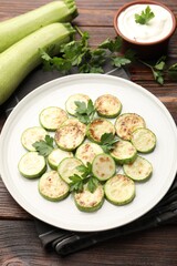Delicious fried courgette slices with parsley served on wooden table, closeup