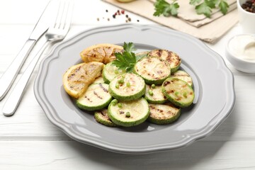 Delicious fried courgette slices with lemon, green onion and parsley served on white wooden table, closeup
