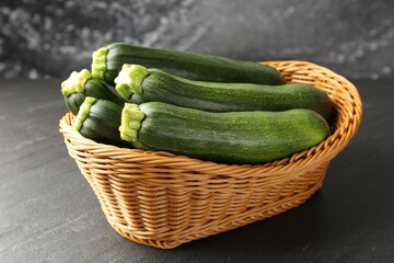 Fresh ripe zucchinis in wicker basket on black table, closeup