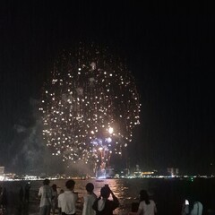 A stunning display of bright white fireworks exploding in the night sky over a body of water. The light from the fireworks reflects on the gently rippling surface of the water. The distant city  