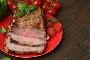 Delicious baked beef meat, tomatoes and basil on wooden table, closeup. Space for text
