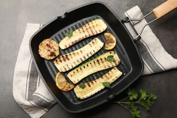 Delicious grilled courgette slices with garlic, lemon and parsley in pan on grey textured table, flat lay