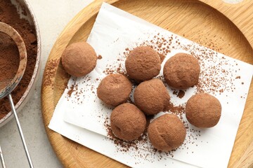Tasty chocolate candies with cocoa powder and strainer on light table, flat lay