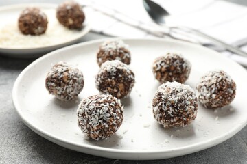 Tasty chocolate candies with nuts and coconut flakes on grey table, closeup