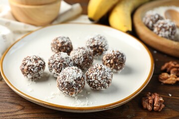 Tasty chocolate candies with nuts and coconut flakes on wooden table, closeup