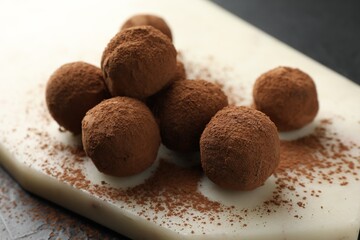 Tasty chocolate candies with cocoa powder on black table, closeup