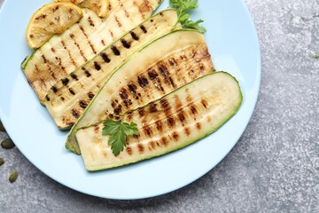 Delicious grilled courgette slices with parsley and lemon on gray textured table, flat lay