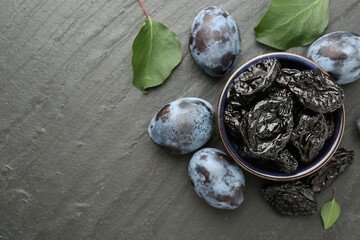 Dried prunes and fresh plums on black table, flat lay. Space for text