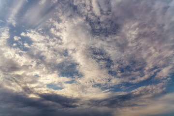 White and gray clouds high in the sky with play of light and shadow, vast colossal sky with clearings in clouds, light in the heavens, panoramic sky landscape with clouds
