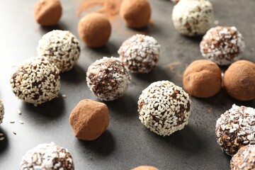 Tasty chocolate candies with cocoa powder, nuts, coconut flakes and sesame seeds on grey table, closeup