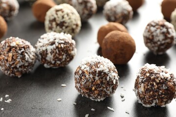 Tasty chocolate candies with cocoa powder, nuts, coconut flakes and sesame seeds on grey table, closeup