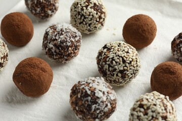 Tasty chocolate candies with cocoa powder, nuts and sesame seeds on white board, closeup