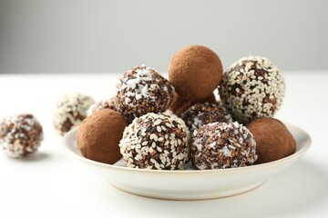 Tasty chocolate candies with cocoa powder, nuts and sesame seeds on white table, closeup