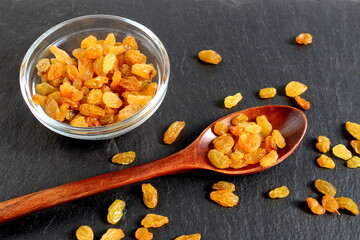 On a black background there is a glass cup with a wooden spoon with raisins.	