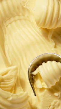 Butter is scraped off with a special butter knife from a pack of butter into a recognizable round shape. Extreme macro close-up, perfect for culinary and advertising projects.