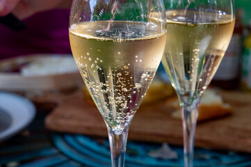 Two fluite glasses of sparkling white wine with bubbles champagne in sunny garden with old iron furniture on French village in Cote des Bar, Champagne region, France in summer