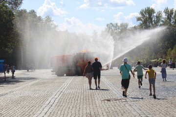 A watering machine drives around the city square and refreshes people.