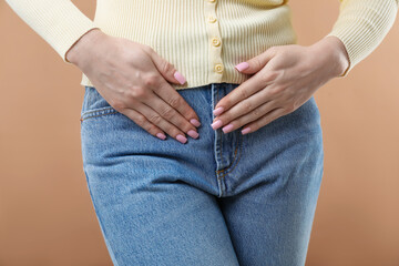 Woman suffering from cystitis symptoms on dark beige background, closeup