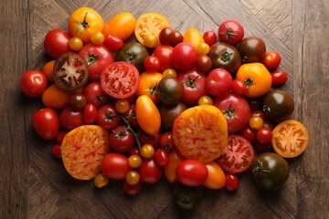 Many different ripe tomatoes on wooden table, flat lay
